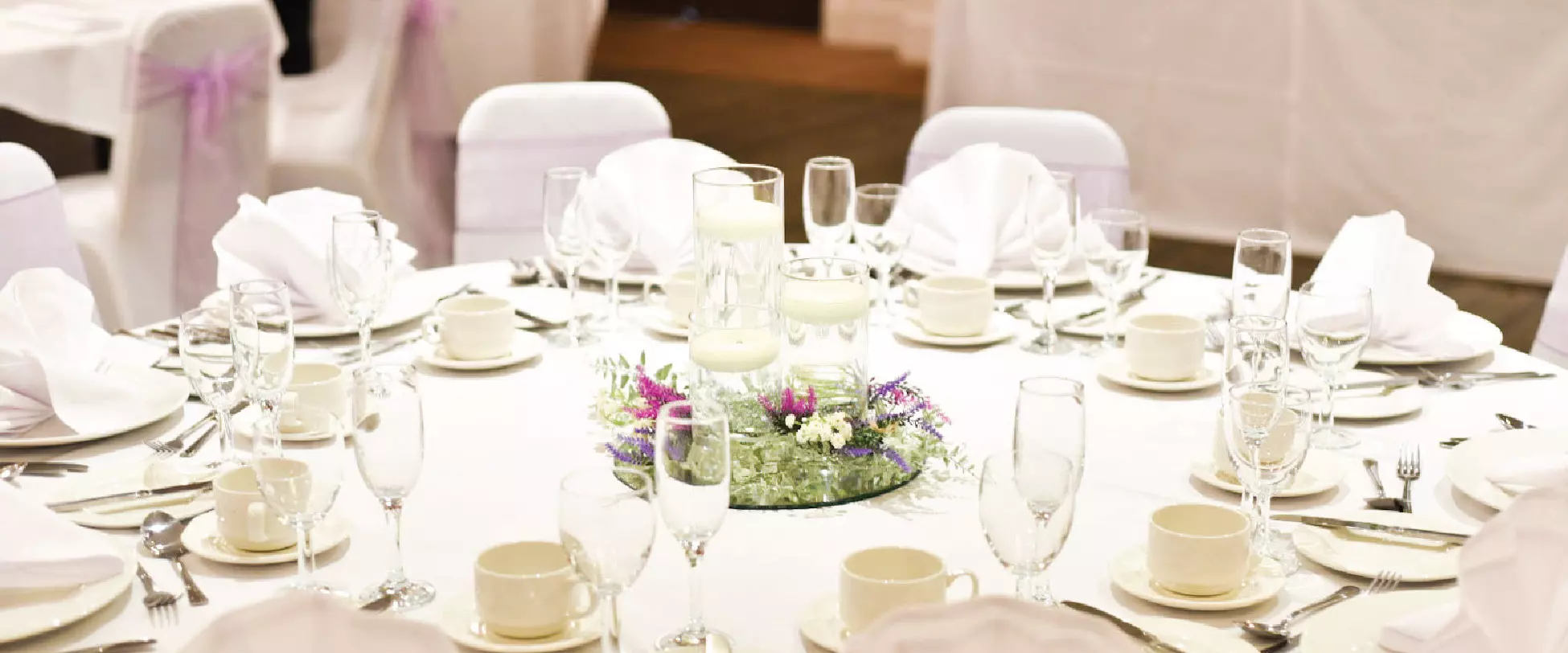 A circular wedding table dressed for a wedding with a centrepiece of pink and purple flowers.
